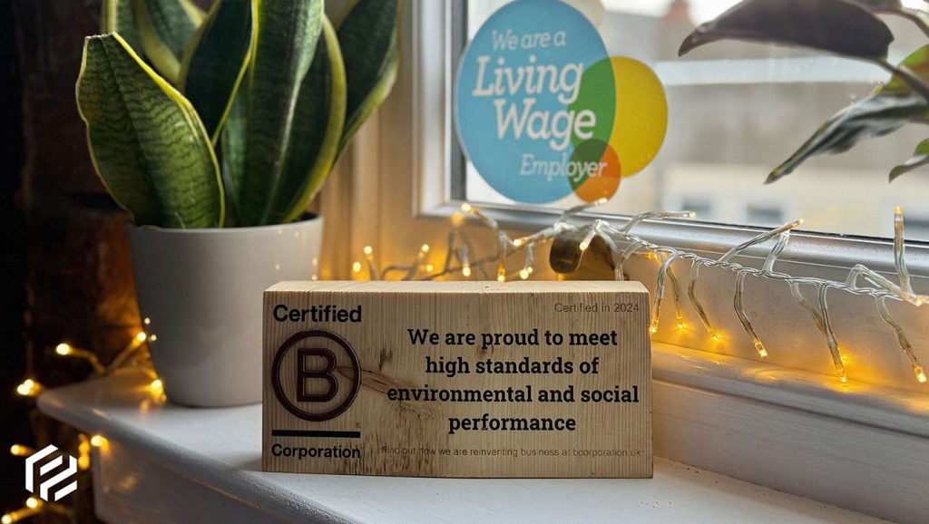 Our B Corp plaque in front of our Living Wage sticker on the windowsill in the office - Phonetic Digital